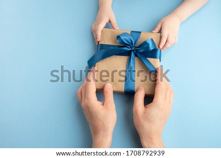 Fathers day, birthday and holiday concept. Little child gives his father gift on light blue background. Top view, flat lay, copy space