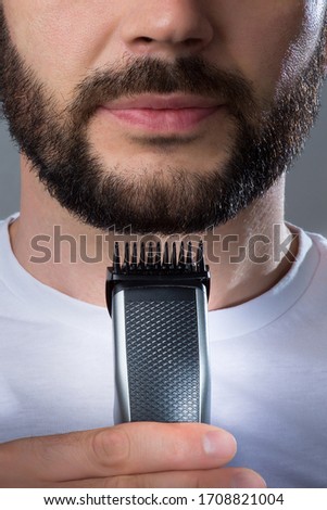 A man holds a trimer near his beard