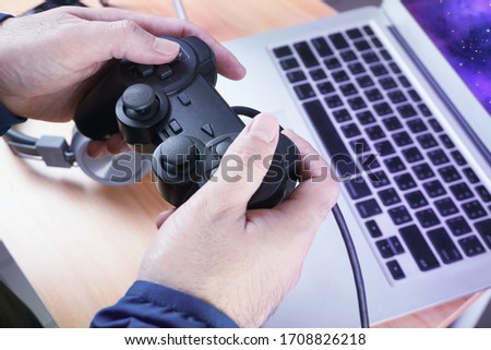 Gamer holding controller joystick on hands and play game with background laptop screen , e-sport concept.