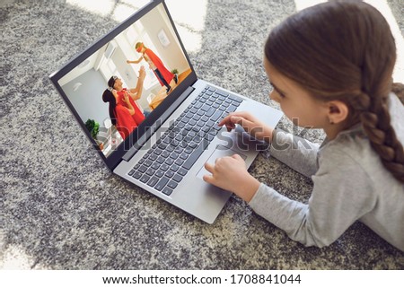 A child uses a laptop to watch home videos in a room on the floor.