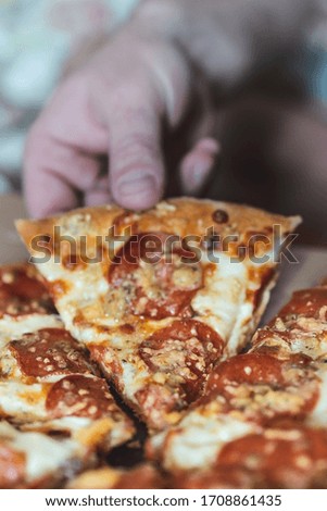 Cropped man takes a piece of pizza with his hand. Selective focus, blur, closeup.