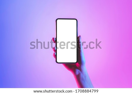 Hand holds smartphone with blank screen in neon, free space