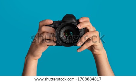 Close up of photographer pointing DSLR camera at screen, blue background. Panorama