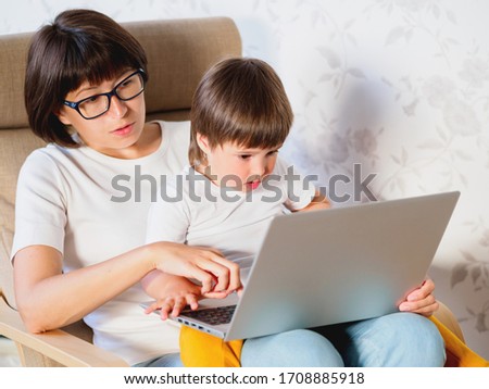 Mother and her toddler boy sit together on chair with laptop. Woman tries to remote work, but kid is asking for game or cartoons. quarantine lockdown because of coronavirus COVID-19.