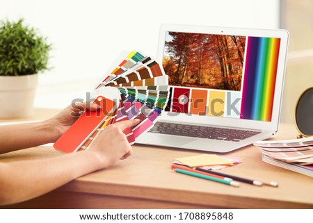 Professional female designer working with color palette samples and laptop at desk, closeup 
