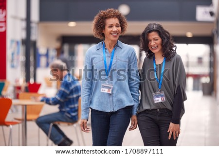 Two Mature Female Students Or Teachers Walking Through Communal Hall Of Busy College Campus Building Royalty-Free Stock Photo #1708897111