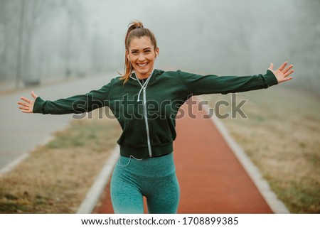 Close photo of young excited woman runner with beautiful smile and outstretching arms after outdoor run on foggy morning.