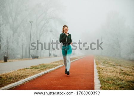 Wide angle photo of pretty sporty woman jogging outdoor on foggy morning.