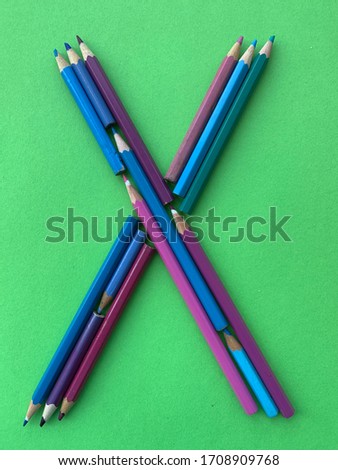 The letter X is laid out from colored pencils on a background of turquoise-green  paper.