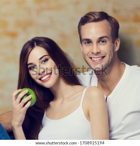 Happy toothy smiling beautiful couple with apple, against loft style wall. Vegetarian, weight lossing, dieting, healthy food and dental health concept. Square composition.