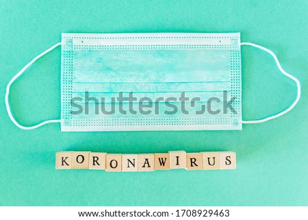 Word written with wooden blocks with black letters laying on protective surgical masks. "Koronawirus" means "coronavirus" in polish.