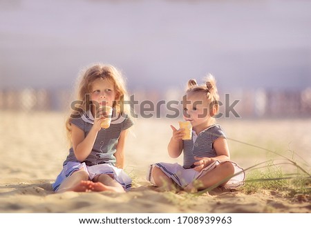 Two cute sisters in the same sea dresses eating an ice cream on the beach