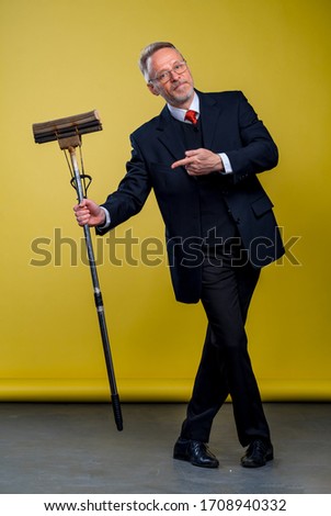 Senior man in suit holding a boom. Manager man pointing at mop in studio.