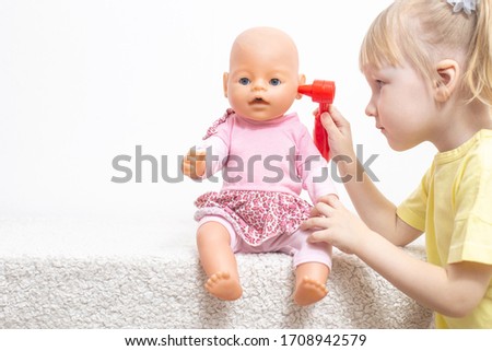 A little girl plays with a doll examines her ears. The concept of pediatric otolaryngology in medicine, treatment of otitis media and sulfur caps in children, copy space, damage Royalty-Free Stock Photo #1708942579