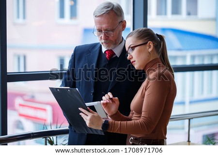 Girl manager in her own office tells a successful new business plan for economic development to her teacher mentor boss. Holds a folder with important documents in his hands.