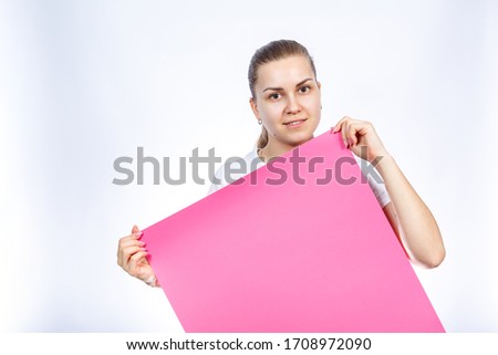 A girl in a white T-shirt is holding a pink blank large sheet of banner in her hands.