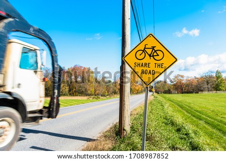 Warning road sign telling drivers to share the road with bicycles along a busy country road on a sunny autumn morning