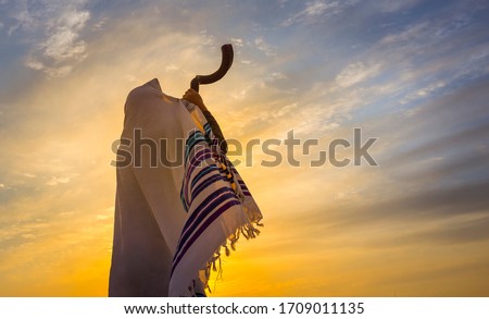 Blowing the shofar for the Feast of Trumpets - Jewish man in a traditional tallit prayer shawl blowing the ram's horn against dramatic sunset sky Royalty-Free Stock Photo #1709011135
