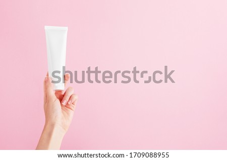 Unbranded flacon for cream, concealer, toiletry. Plastic tube in female hand. Container for professional cosmetics products. Skincare and beauty concept. Mockup, copy space. Isolated on pink Royalty-Free Stock Photo #1709088955