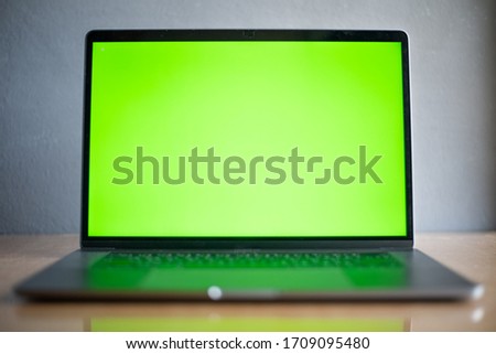 Laptop with green screen on wood table on blur background in technology concept.