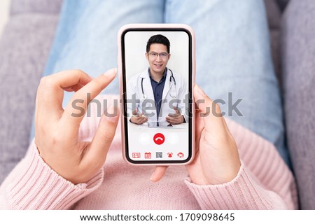 Asian chinese doctor or therapist help releave stress from coronavirus crisis video conference call online live talk remotely with woman sit on sofa couch at home using smartphone doctor consultation. Royalty-Free Stock Photo #1709098645