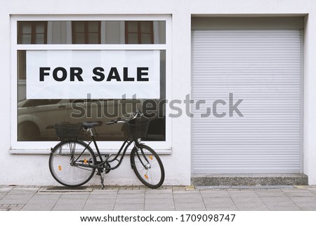 for sale sign in store window with bicycle parked outside - shop vacancy due to business closure - economy crisis and recession concept