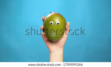 Mango with eyes in a woman hand on a blue background. Woman hand close-up.