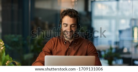 Businessman smiling and talking with a client over a headset while working alone at his desk in a dark office after hours Royalty-Free Stock Photo #1709131006