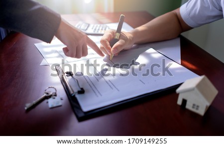 Realtor pointing at the signing of the contract document about house purchase agreements, rentals, bank loan, real estate on table with background sunlight from window. Concept of Investment property.