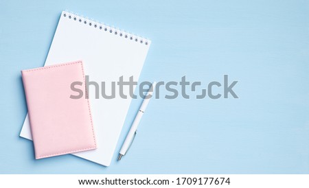 Blank notepad with pen and documents on blue background. Flat lay, top view office desk. Minimal style feminine workspace