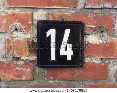 House sign number 14: black square plate with white digits against a brick wall