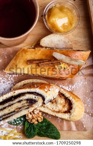 Poppy strudel is decorated with powdered sugar, cinnamon, nuts and mint and tea in a paper cup. Homemade cake with natural ingredients. Rustic wooden background. Top view. Flatlay.