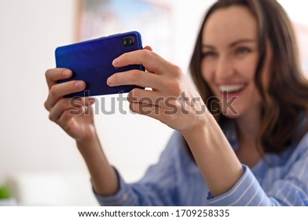 closeup one smiling woman in blue shirt talks on phone, video calls, takes selfies, online game, communication in quarantine concept