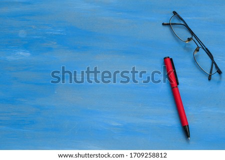 Pen and glasses on the blue background.