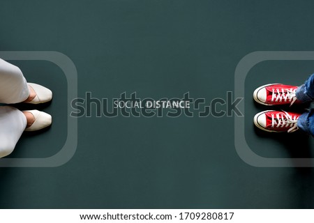 Two people standing with the word social distance in between border line. Concept of staying physically apart for infection control intended to stop or slow down the spread of COVID-19 coronavirus. Royalty-Free Stock Photo #1709280817