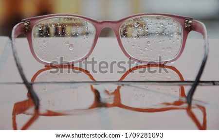 close up of modern eyeglasses with raindrops  laying on the reflective surface with the city view 
