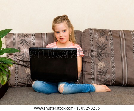 Distance learning. Smiling little girl sitting on a sofa with a laptop, watching a cartoon or making a video call on a computer