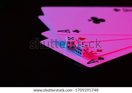 Playing cards of four aces with dice in neon blue-pink light on a black background. Game addiction. Poker