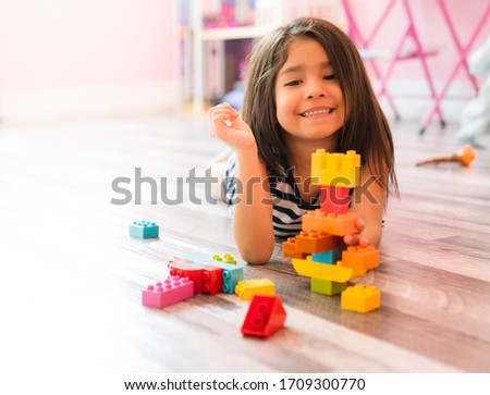 Portrait of a cute happy little preschool Hispanic girl playing alone with colorful construction blocks in her bedroom floor at home. Child Developing Motor Skills With Games Copy Space Royalty-Free Stock Photo #1709300770