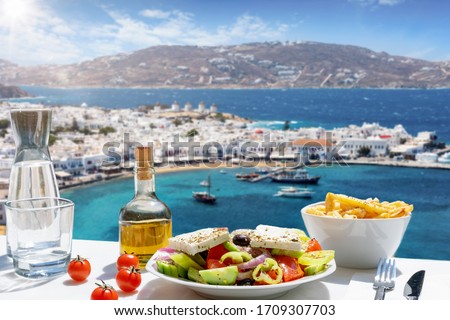 Tasty Greek food with salad, feta cheese and olive oil served with a view to the beautiful island of Mykonos, Greece, during summer time