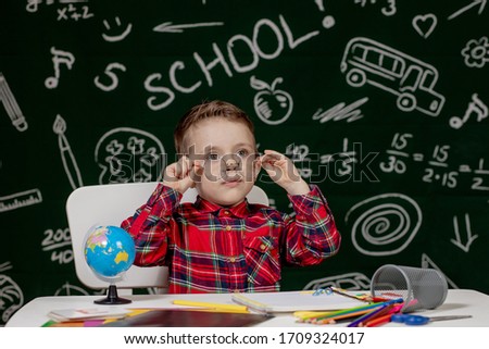 Emotional school boy sitting on the desk with many school supplies. First day of school. Back to school