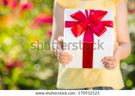 Child holding gift box against green background. Spring family holiday concept. Mother`s day