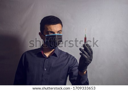 Doctor standing with stethoscope holding a syringe on a gray background
