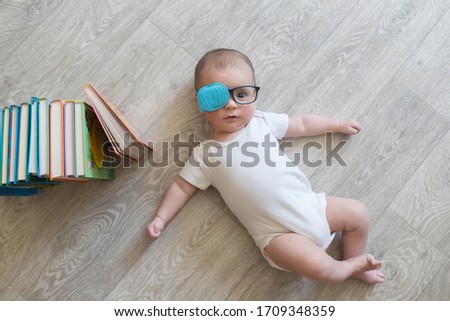 Newborn baby in glasses with books. A little boy in white clothes and blue . Beautiful portrait of a toddler. Big-eyed baby. Remote education. Distance learninig. Treat lazy eye, amblyopia, strabismus Royalty-Free Stock Photo #1709348359