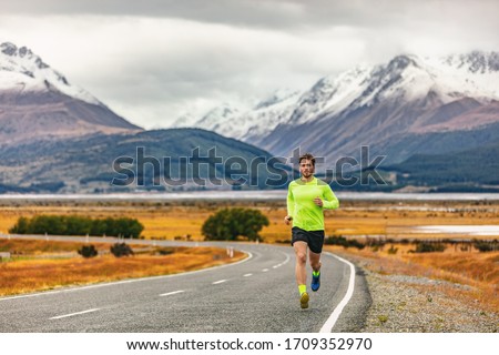 Athlete runner running road race in amazing mountain range landscape in New Zealand. Man run exercise long distance cardio training outdoors in cold fall weather. Royalty-Free Stock Photo #1709352970