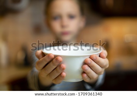 Unrecognizable child girl reaching out hands holding white empty bowl plate offering food or asking for food. Shallow focus. Giving concept. Hungry children Royalty-Free Stock Photo #1709361340