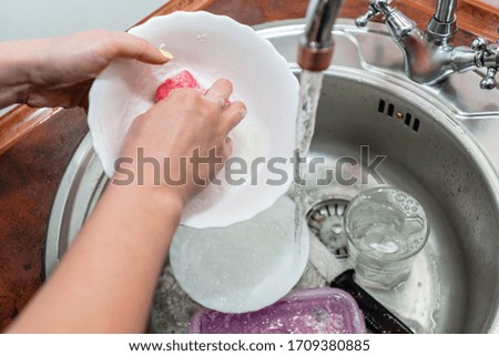 Close up hands of woman washing dishes in kitchen. Cleaning chores