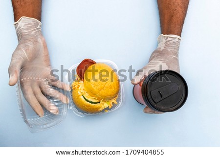 doctor wearing surgical gloves on a plain background, with a hamburger for lunch, concept