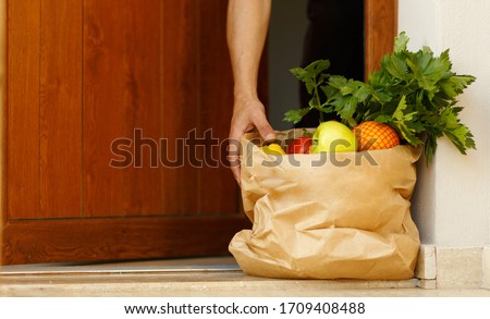 home delivering some groceries at quarantine of coronavirus infection COVID-19. hand of man taking shopping bag at front door. Food delivery in shopping bag. neighborhood Assistance during Pandemic Royalty-Free Stock Photo #1709408488