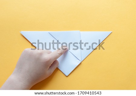 Step 7. Hands of a child on a yellow background divide a square of white paper into triangles. Origami bull concept.